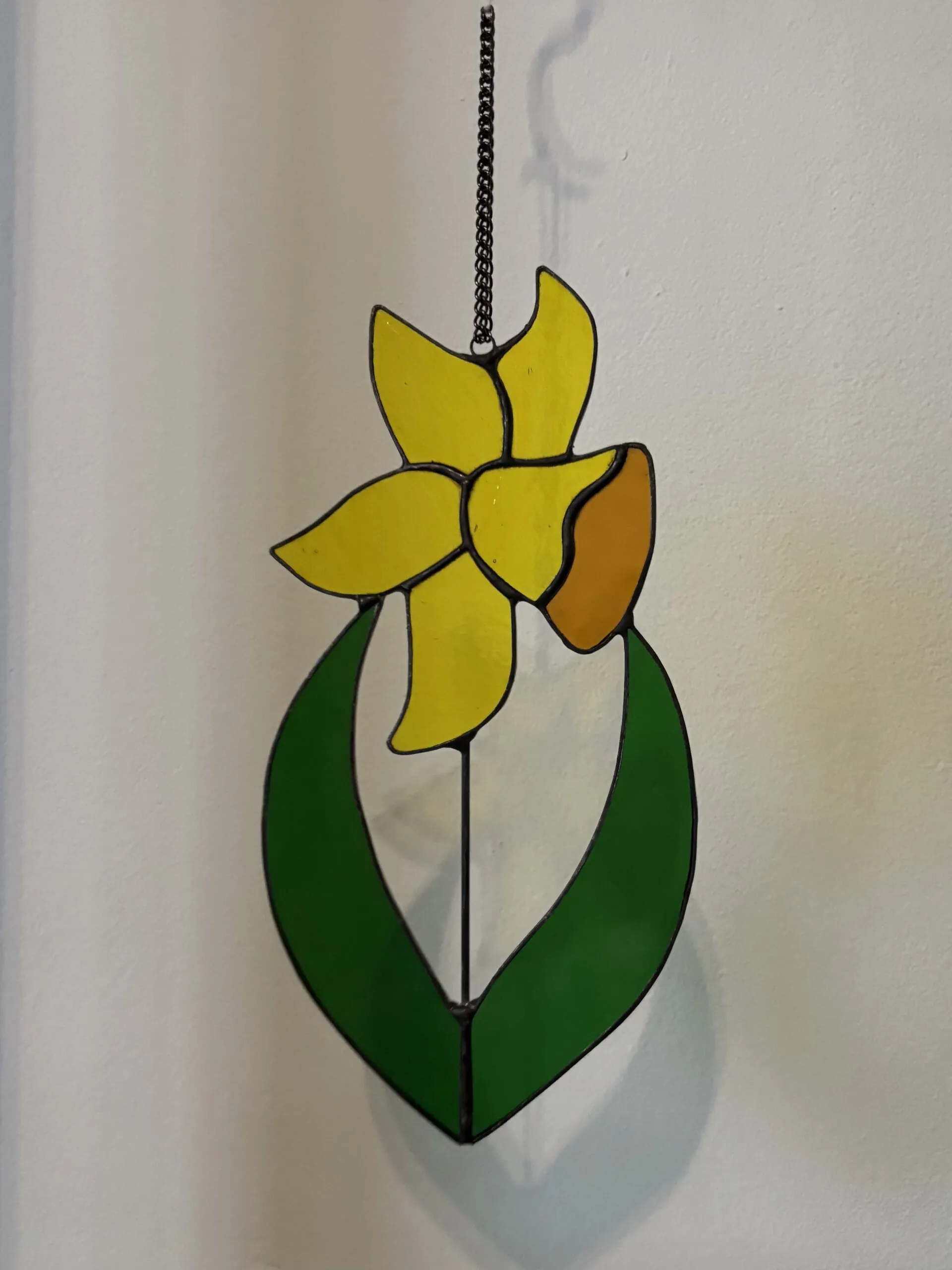Glas in lood hanger: een gele narcis met donker groene bladeren.