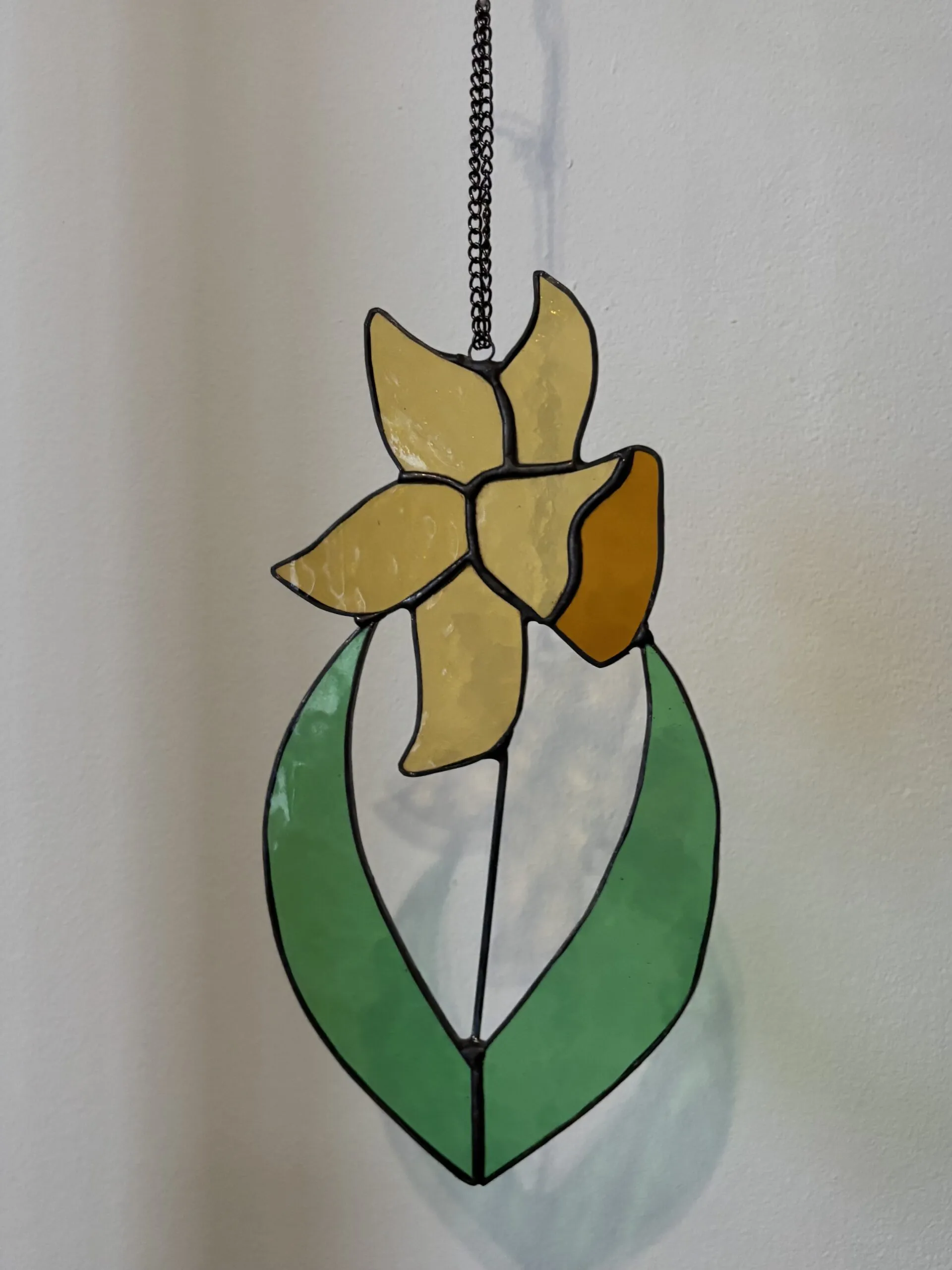 Glas in lood hanger: een gele narcis met licht groene bladeren.