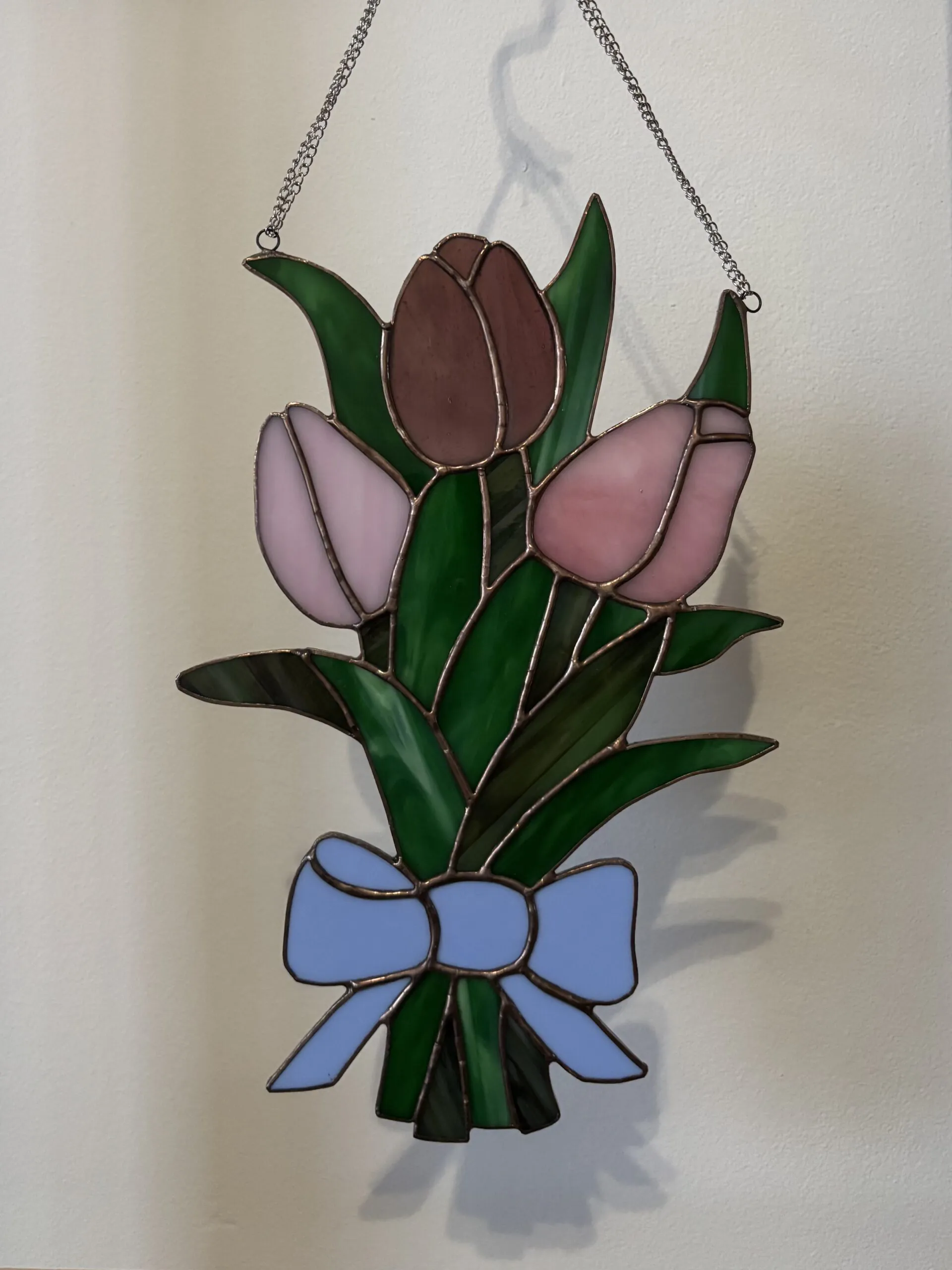 Glas in lood tulpen: een bosje tulpen in roze en paarse tinten. Met groene blaadjes/takjes en een blauwe strik.