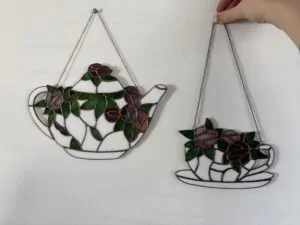 Glas in lood hanger: witte theepot met roze en paarse bloemen en een bijpassend wit kopje met schotel ook met roze en paarse bloemen.